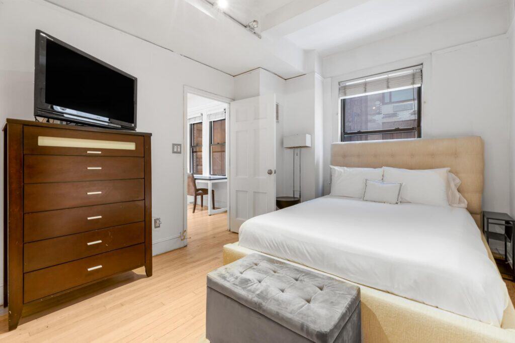 Bright bedroom with a large bed, dresser, and window letting in natural light.