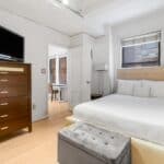 Bright bedroom with a large bed, dresser, and window letting in natural light.