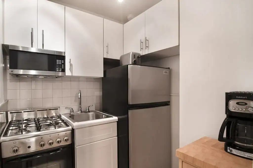 Compact kitchen with stove, refrigerator, microwave, and coffee maker.